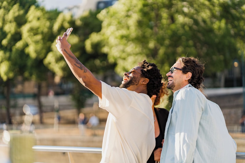Two people taking a selfie outdoors with trees and a railing in the background. 3