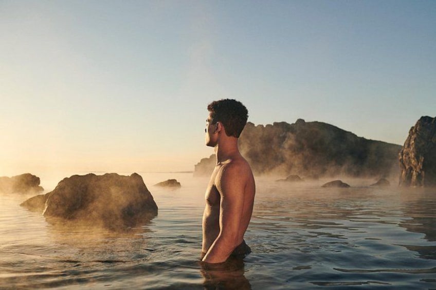 A person standing in a body of water with steam rising from the rocks. 2