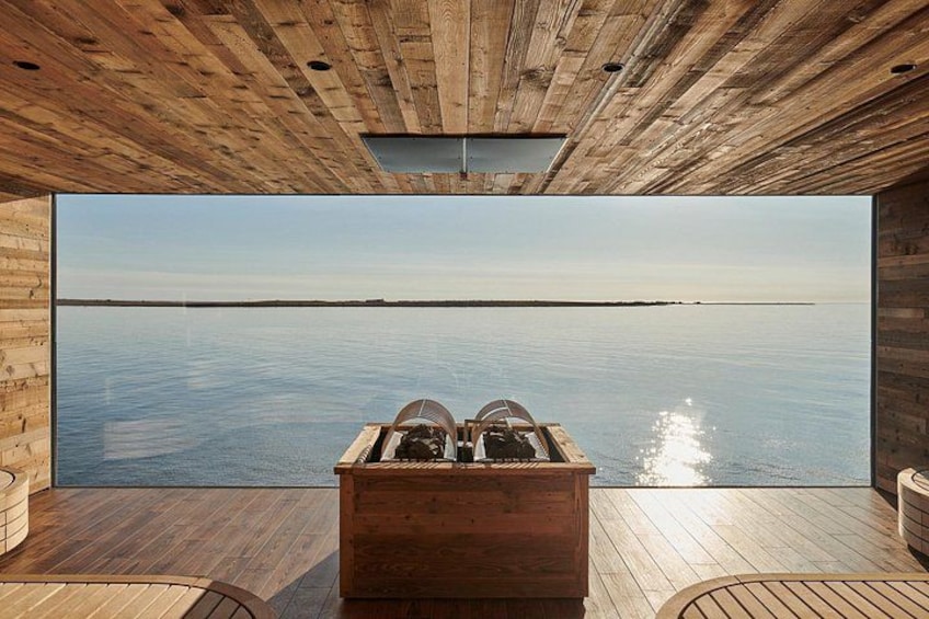 A wooden cabin with a large window overlooking a calm body of water. 1