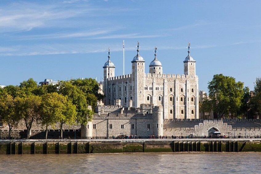 A historic building with multiple towers and domes, a river in the foreground, and trees in the background. 3