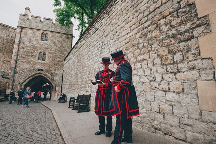 Dos guardias con uniformes tradicionales permanecen junto a un muro de piedra con la entrada de un castillo al fondo. 2