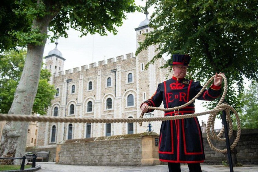Una persona con uniforme sosteniendo una cuerda, de pie frente a un edificio histórico con ventanas de arco y una torre. 3