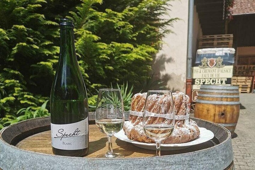 A bottle of Spacht white wine, a glass, and a plate of pastries on a round table outdoors. 2