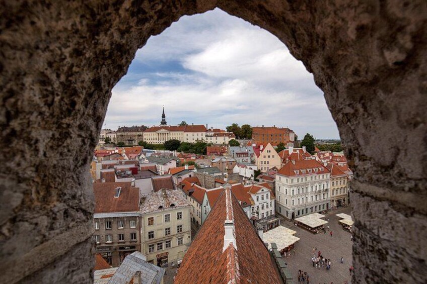 Blick durch ein Portal auf eine Stadt mit roten Dächern, einer markanten Kirche und einer weit entfernten Burg. 1