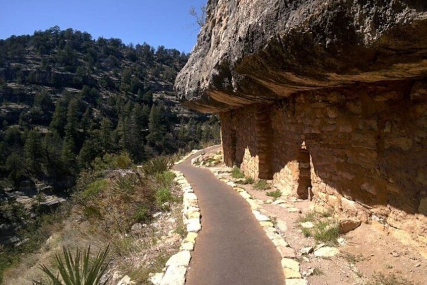 Un sendero pavimentado estrecho al lado de un muro de piedra, con una ladera rocosa al fondo. 1