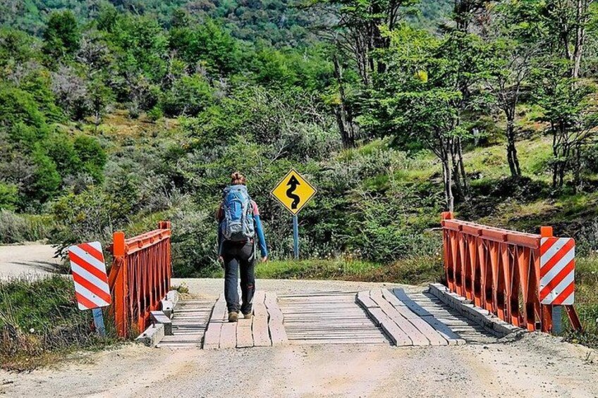 Una persona caminando sobre un puente con un letrero amarillo de advertencia, rodeada de follaje. 3