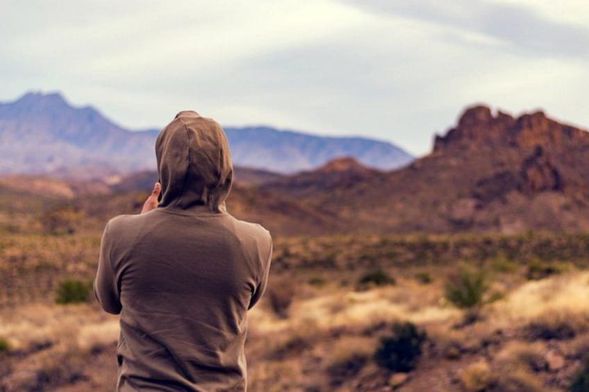 Una persona con sudadera de capucha de pie en un paisaje desértico con montañas al fondo. 4