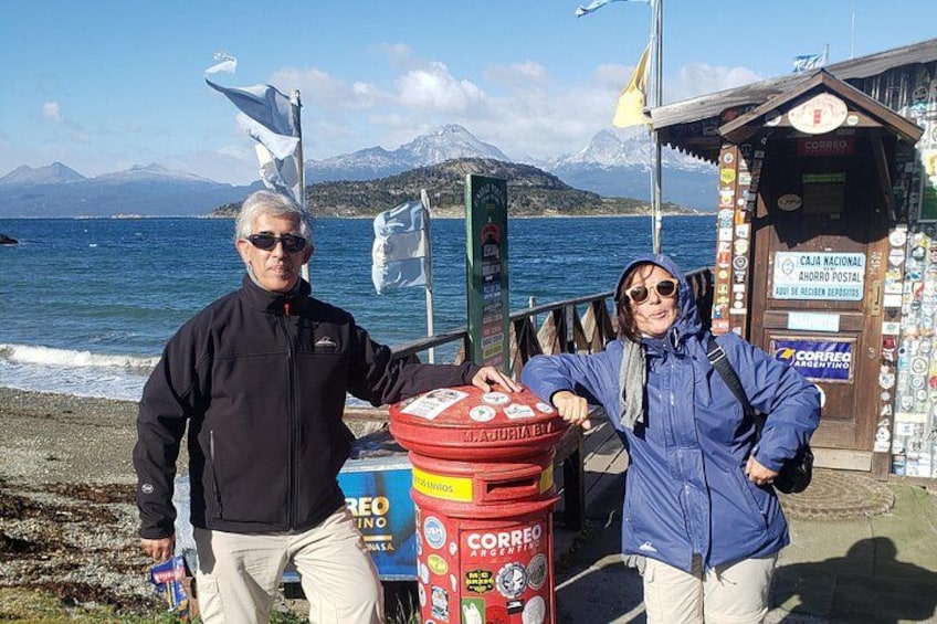 Un hombre y una mujer de pie junto a un buzón en un paseo marítimo con una montaña al fondo. 5