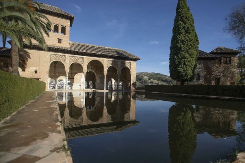 A historic building with arches, a reflective pool, and a tall tree. 4