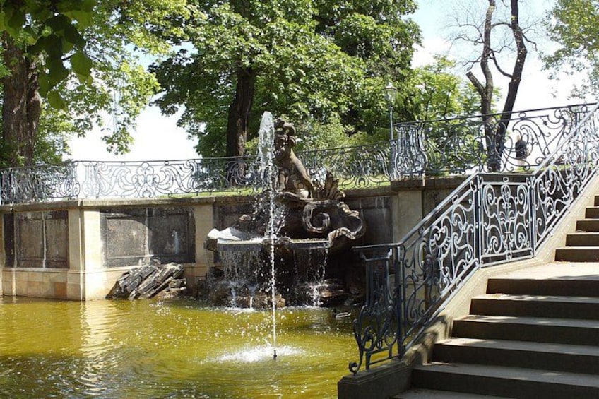 A fountain with water jets, a stone statue, and a wrought iron staircase leading down to a pond. 4