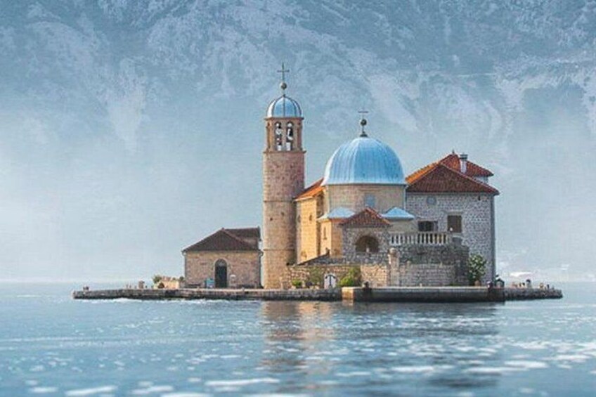 A coastal church with a bell tower and a dome, surrounded by calm waters and a mountainous backdrop. 5