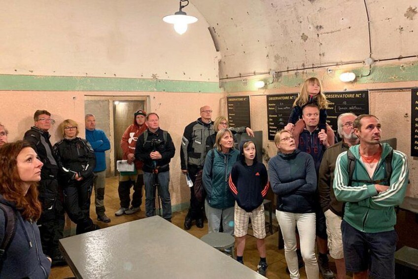 Een groep mensen staat in een ruimte met een tafel en een muur met borden. 2