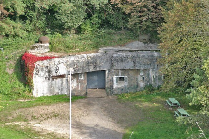 Een betonnen bunker met graffiti, een zandpad en groene banken. 1