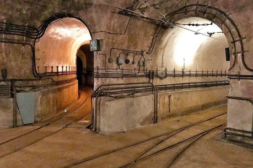 Een ondergronds spoorwegtunnel met gewelfde plafonds, sporen en elektrische leidingen erboven. 4