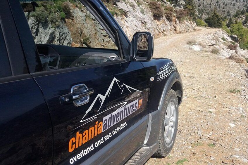 A black SUV with 'Chania Adventures' branding parked on a rocky, dirt road. 5