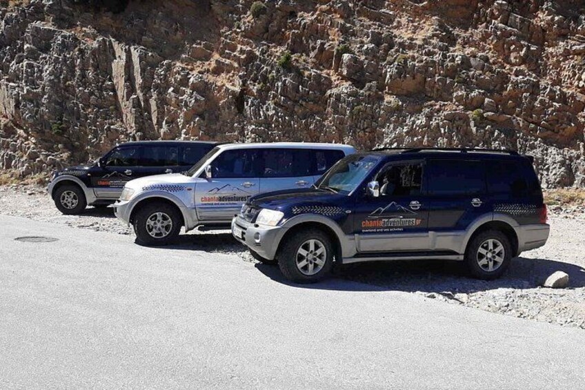 Three off-road vehicles parked on a gravel surface with a rocky hillside in the background. 2