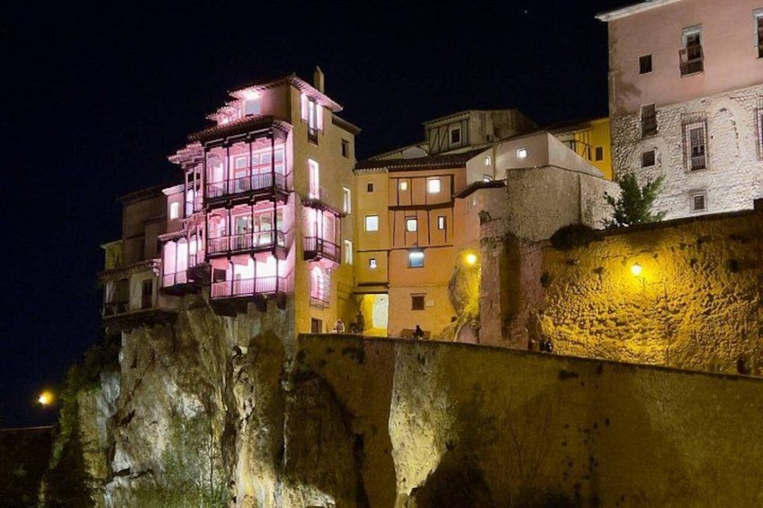 A brightly lit building with balconies, a stone wall, and a rocky cliff. 3