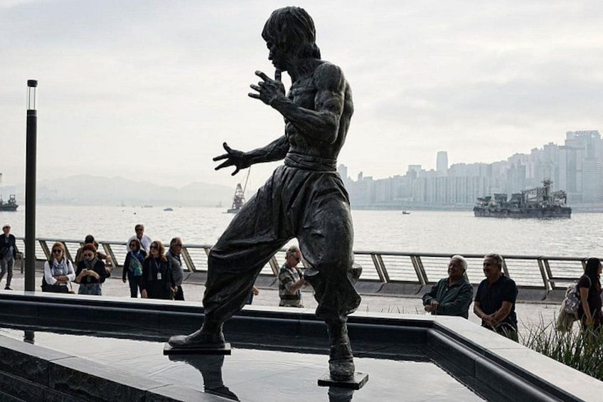 A statue of a man in a dynamic pose, a waterfront with a city skyline in the background, and a few people in the foreground. 4