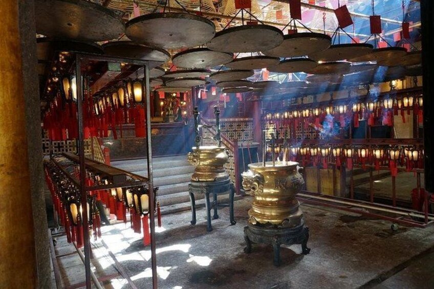 A temple interior with red lanterns, incense burners, and a staircase leading to an upper level. 5