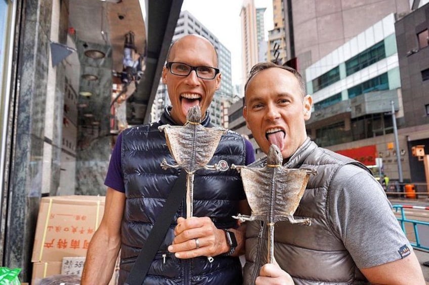 Two people holding fish skeletons in an urban setting with tall buildings in the background. 3