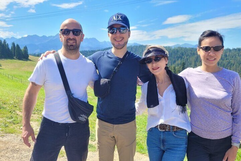 Quatre personnes se tiennent à l’extérieur, avec un paysage montagneux en arrière-plan. 1