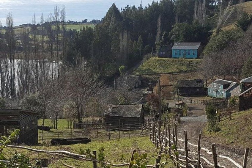 Un paysage rural avec une petite maison sur une colline, une zone délimitée par une clôture et une étendue d'eau en arrière-plan. 2