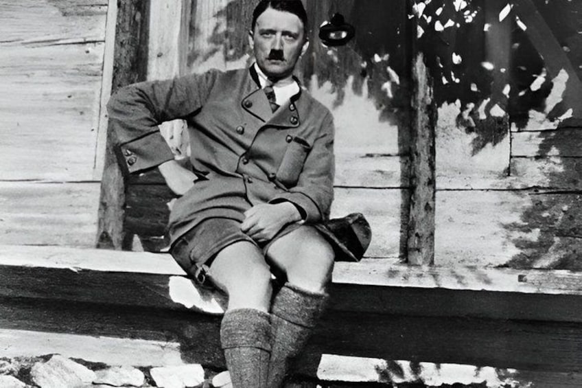 A person sitting on a wooden bench outdoors, wearing a military uniform with a hat and knee-high socks. 1