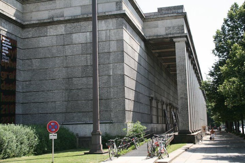 A large stone building with a no parking sign, bicycles, and a tree-lined street. 5