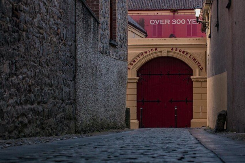 A cobblestone street leading to a red double door with 'Smithwick & Sons Limited' written above it. 3