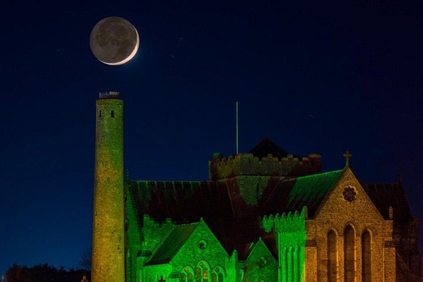 A church illuminated in green, a tower, and a full moon in the sky. 4