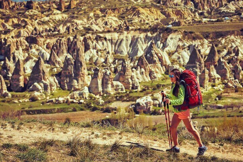 Un excursionista con una mochila roja caminando por un sendero con formaciones rocosas distintivas al fondo. 5