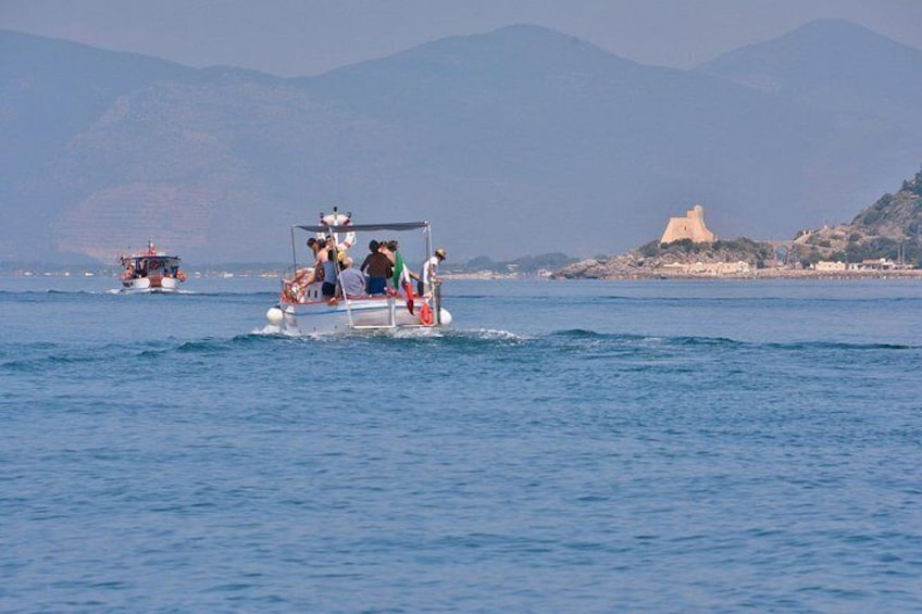 Ein Boot mit Passagieren auf ruhiger See, ein weit entferntes Schloss und Berge im Hintergrund. 3