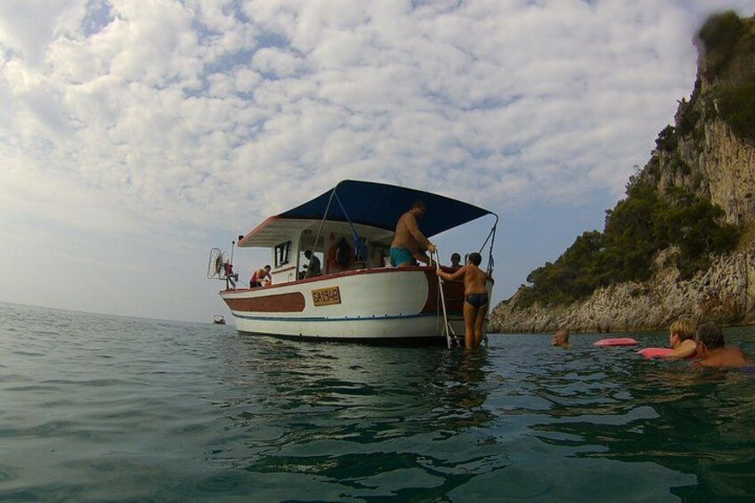 Ein Boot mit Personen auf ruhiger See, eine felsige Küste und ein teilweise bewölkter Himmel. 3