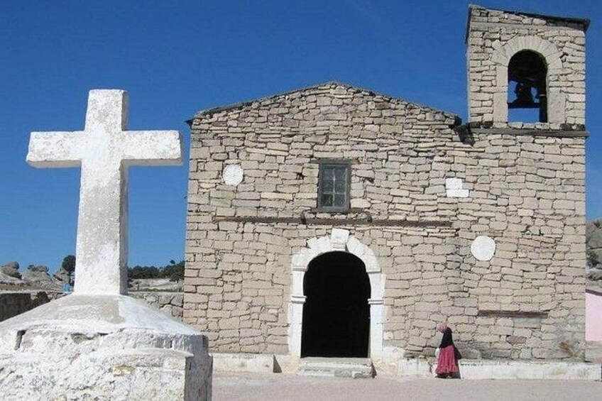 Eine steinerne Kirche mit einem Glockenturm, einem großen Kreuz und einer Person in einem rosafarbenen Kleid. 2