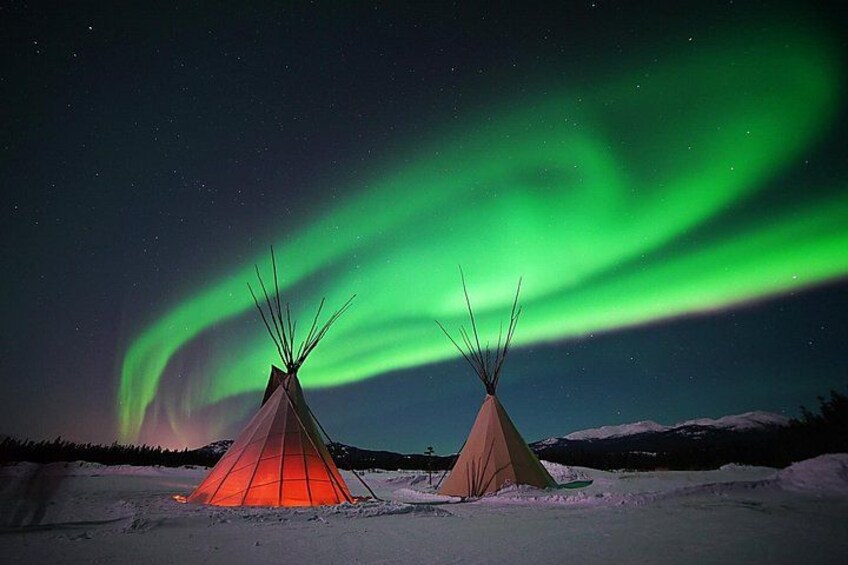 Deux tipis dressés dans un paysage enneigé, sous un ciel nocturne illuminé par les aurores boréales. 2