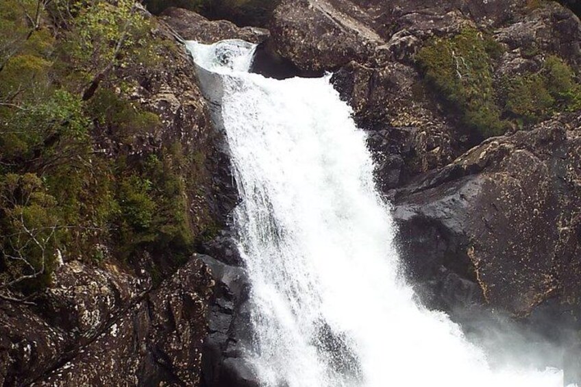 Een waterval stort naar beneden over rotsen in een bebost gebied. 2