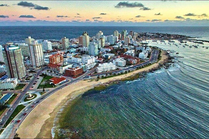 A coastal cityscape with high-rise buildings, a beach, and a marina. 1