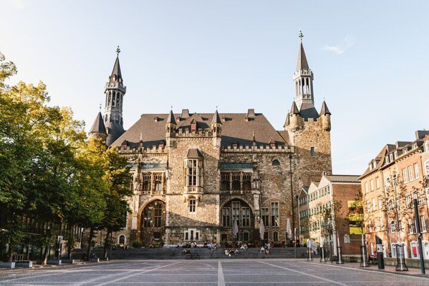 A historic building with two towers, a large open square, and surrounding trees. 2