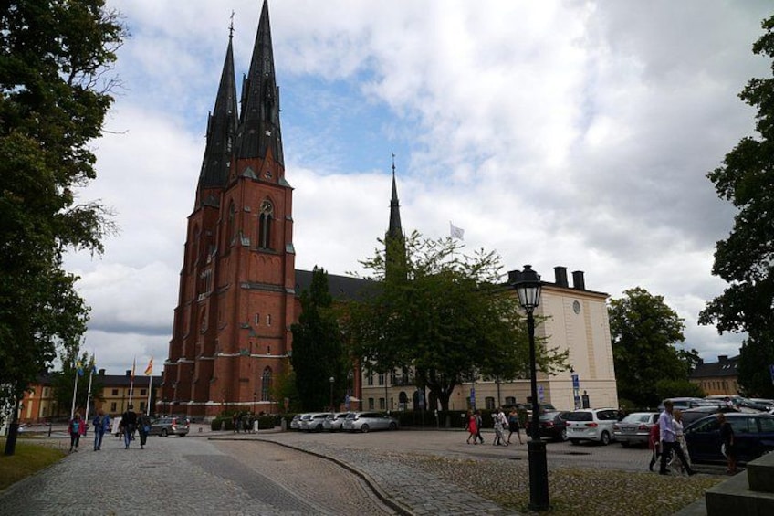 A historic church with a tall spire, a cobblestone street, and a modern building in the background. 1