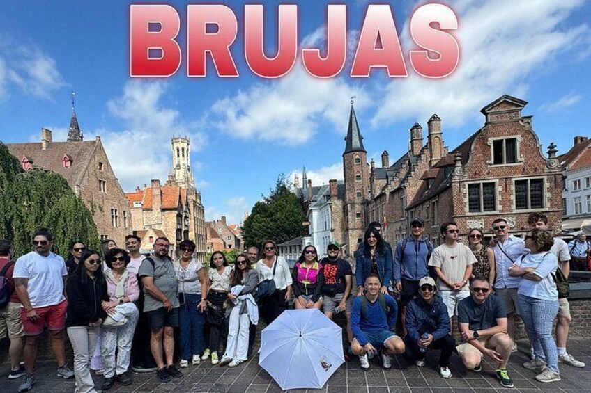 Un groupe de personnes se tient devant des bâtiments historiques, avec le mot « BRUJAS » visible en arrière-plan. 1