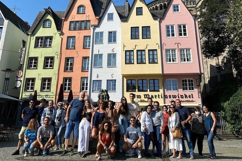 Een groep mensen poseert voor kleurrijke gebouwen, met een bord waarop 'Zum Martinswinkel' staat. 3