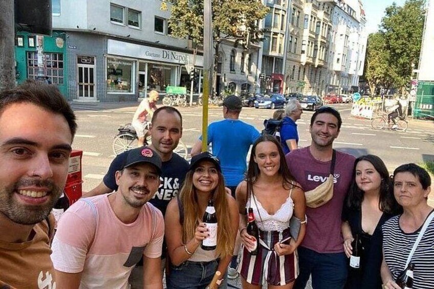 Un groupe de personnes se tient sur une rue de la ville, avec des immeubles et une boîte aux lettres rouge en arrière-plan. 3