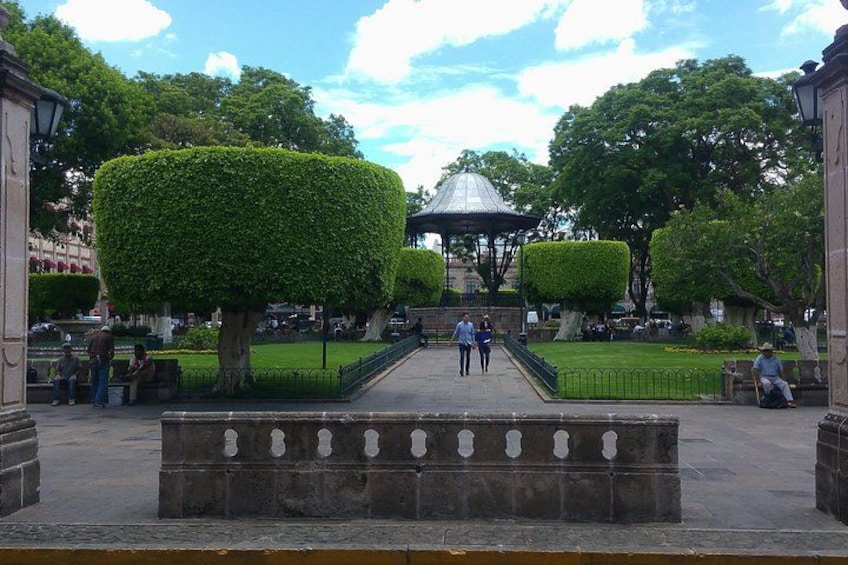 A park with neatly trimmed hedges, a gazebo, and people walking. 3