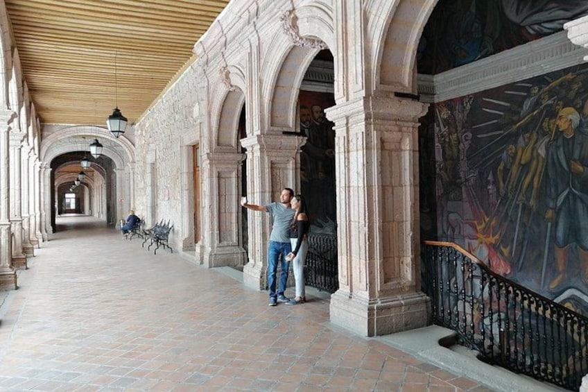 A corridor with arches, a mural, and a person standing. 1