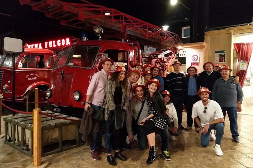 Eine Gruppe von Menschen posiert vor einem roten Feuerwehrwagen mit dem Schriftzug 'FIRE STATION'. 1