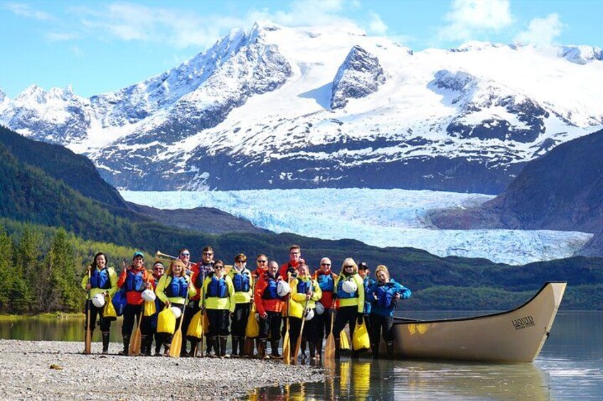 Un grupo de personas con chalecos amarillos junto a un bote en un lago, con montañas nevadas al fondo. 2