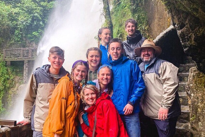 Eine Gruppe von Personen steht vor einem Wasserfall, im Hintergrund eine Stebrücke. 5