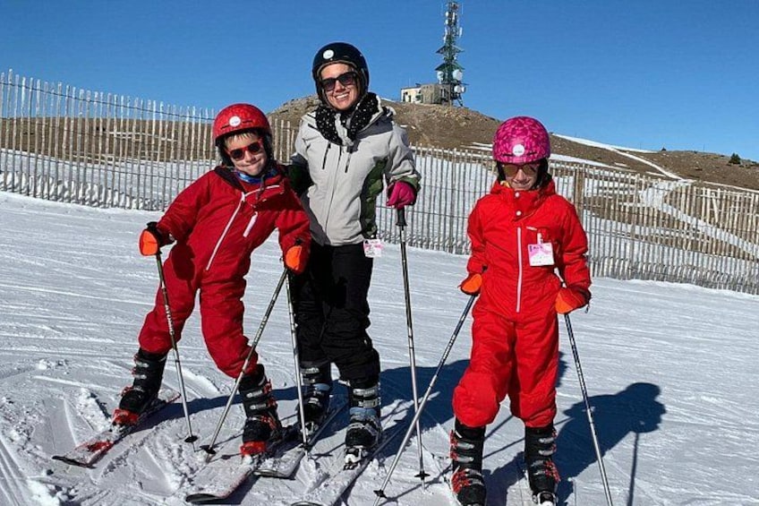 Three people skiing on a snowy slope with a fence and a hill in the background. 3