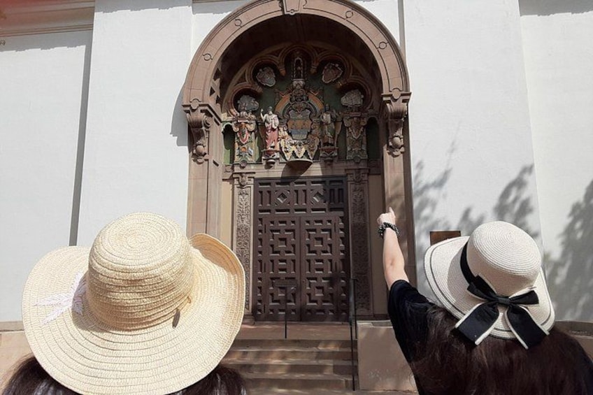 Une personne tend la main vers une porte ornée de sculptures complexes, au-dessus de laquelle se trouve une icône religieuse. 5