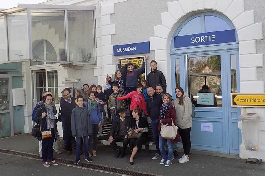 A group of people standing in front of a building with signs reading 'MUSSIDAN' and 'SORTIE'. 1
